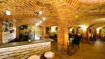 Zona de bar con paredes de ladrillo, taburetes y una barra, rodeada de paredes de piedra e iluminación empotrada.