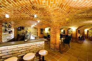 Eine Bar mit Backsteinwänden, Tischen und einer Theke, umgeben von Steinwänden und eingelassener Beleuchtung.