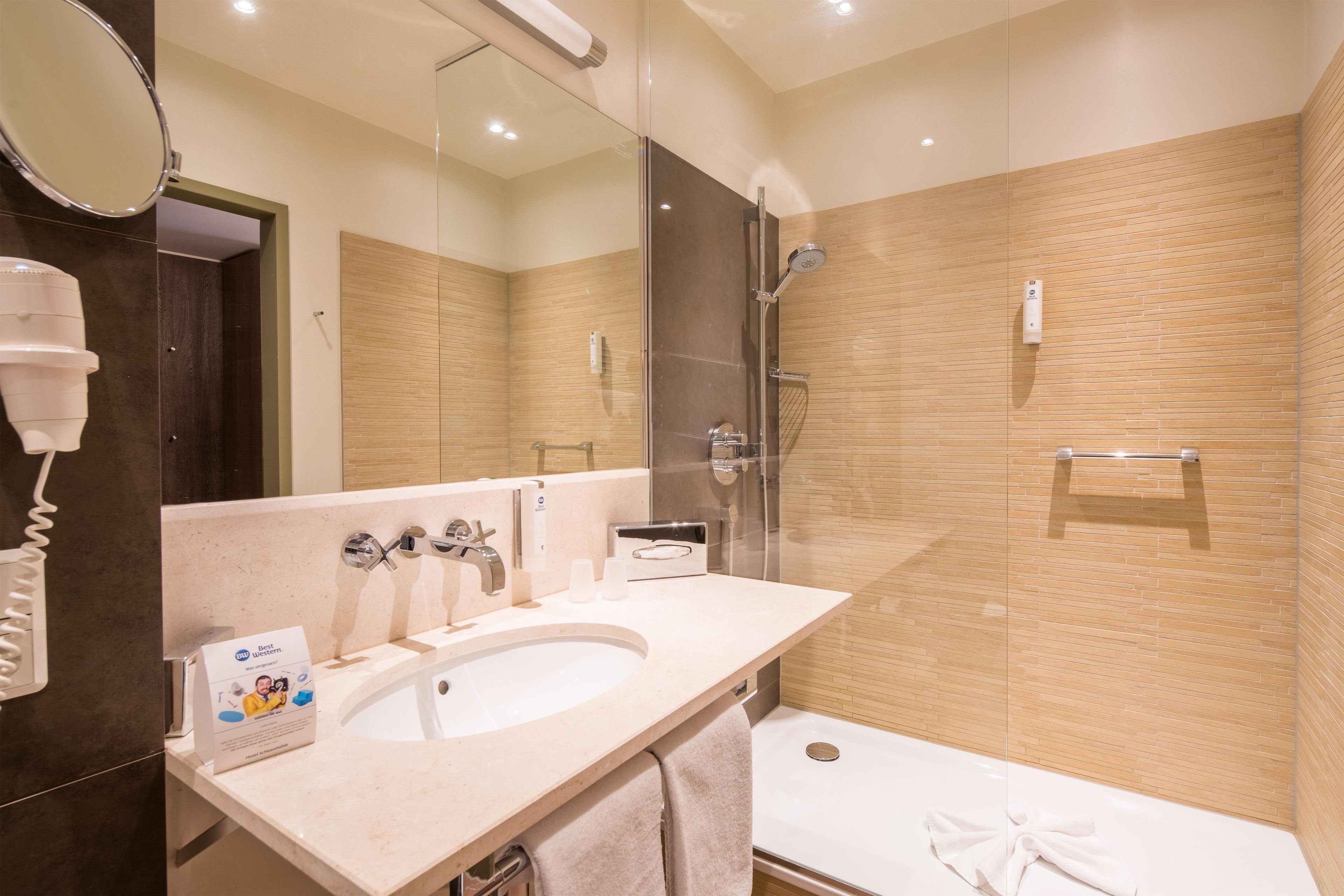 A modern bathroom with a large mirror, a sink, a shower, and a towel rack.
