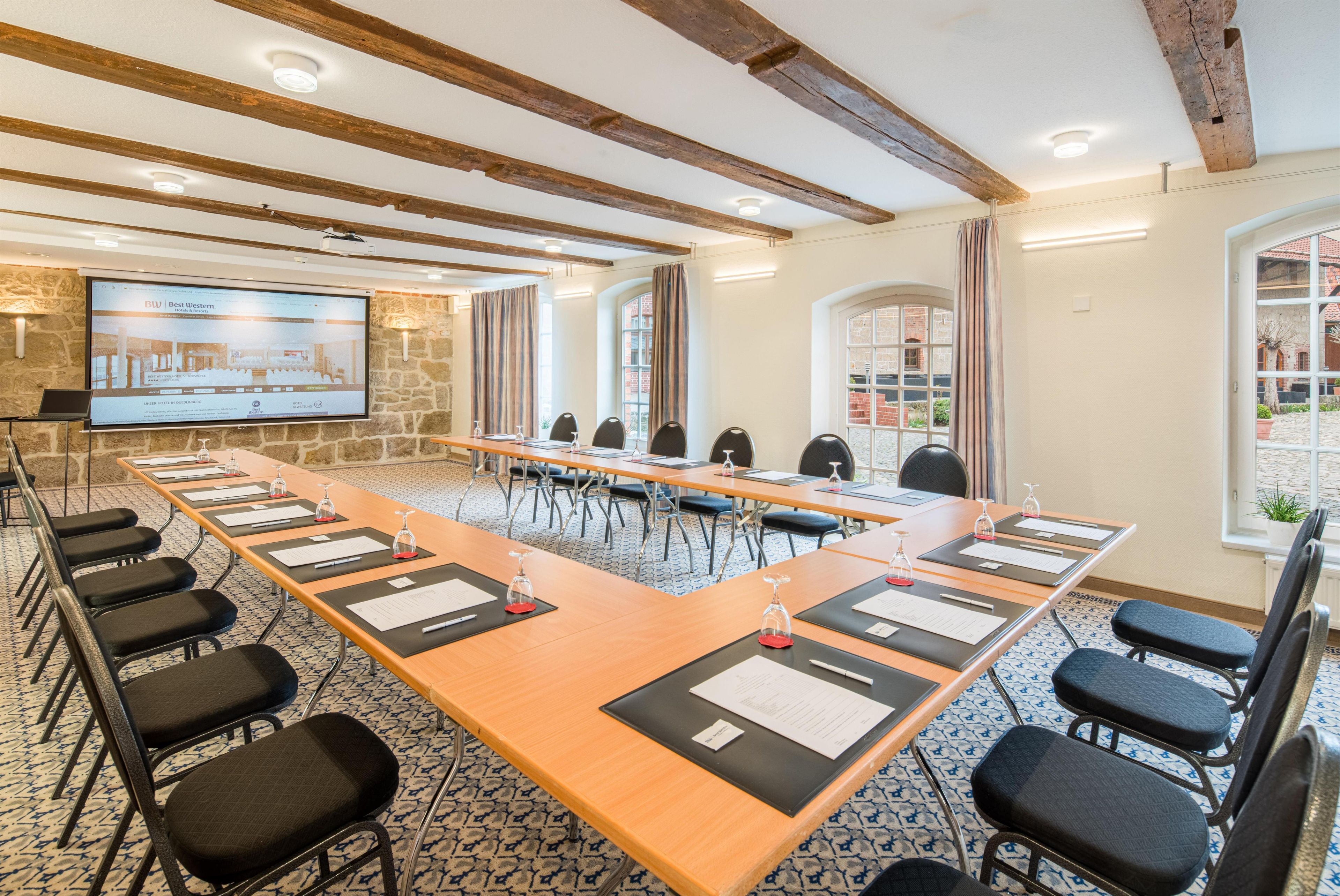 Un salón de conferencias con una larga mesa, sillas y una pantalla que muestra información del hotel.