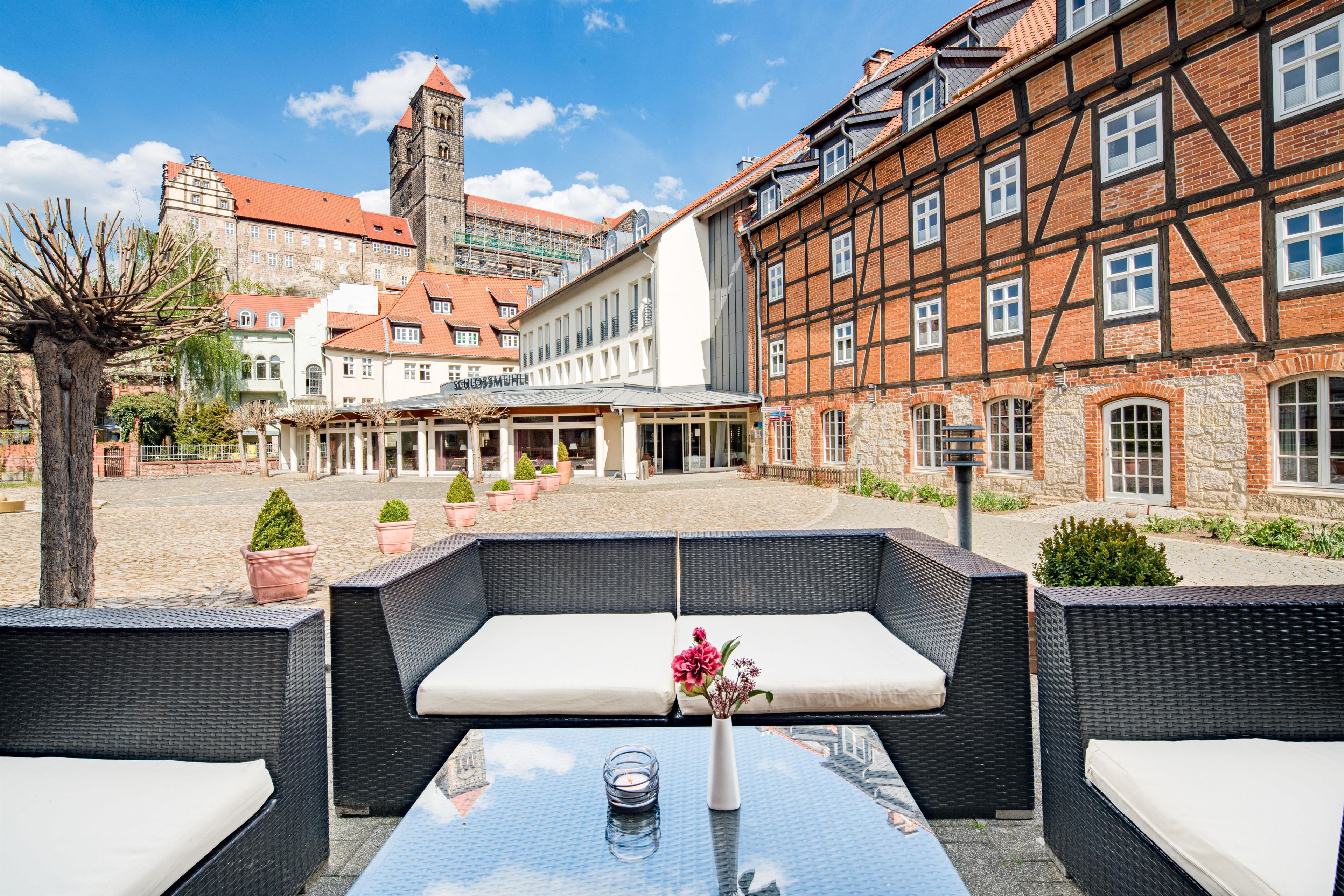 An outdoor seating area with wicker furniture and a table, surrounded by cobblestone pavement and potted plants.