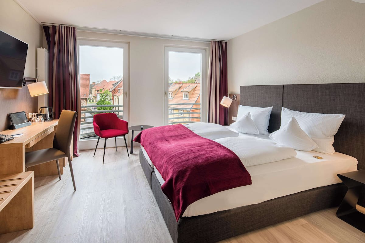Une chambre d’hôtel avec un lit, un bureau, une chaise, une télévision et une fenêtre avec des rideaux.