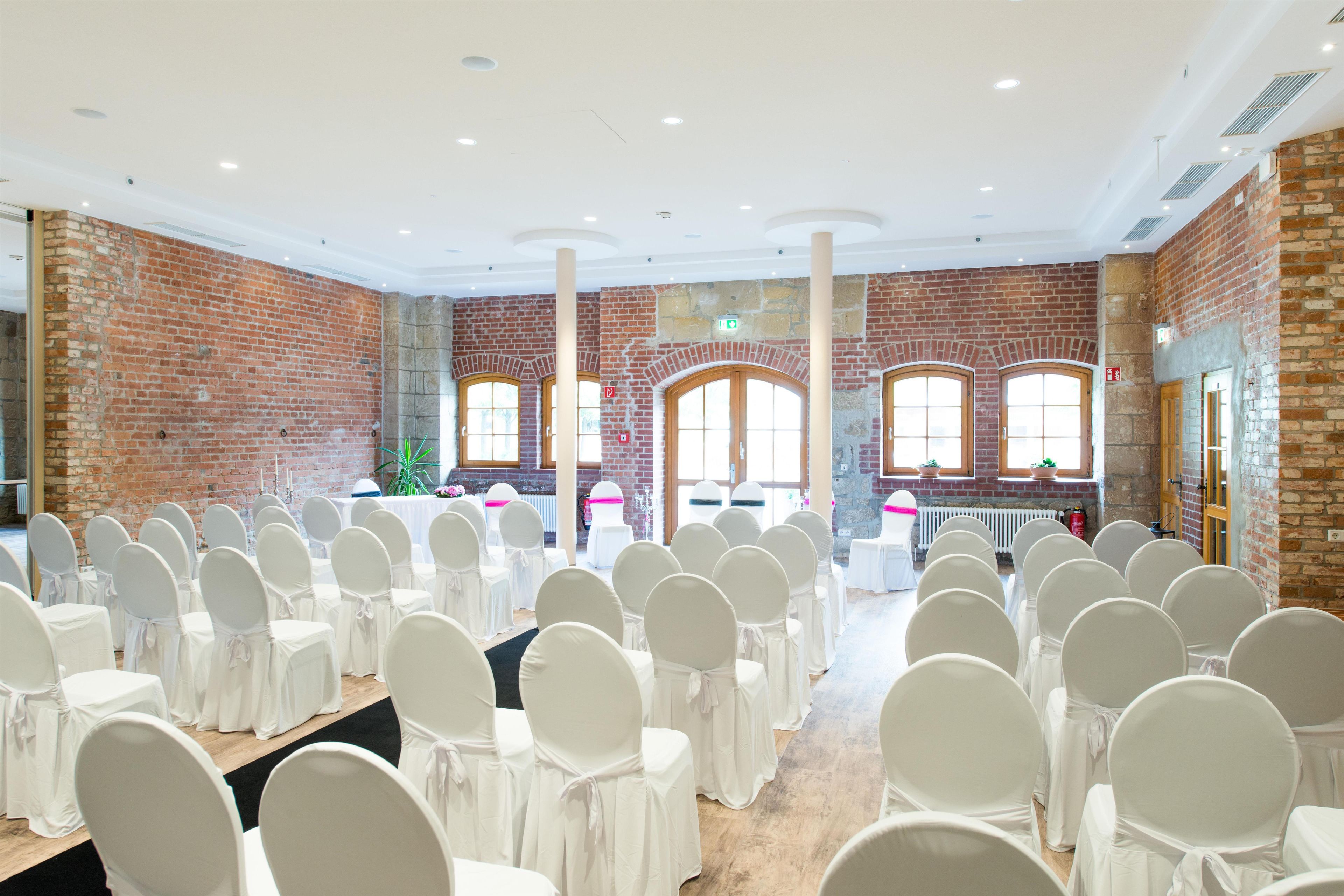 A large hall with rows of white chairs, brick walls, and large windows.