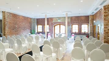 A large hall with rows of white chairs, brick walls, and large windows.