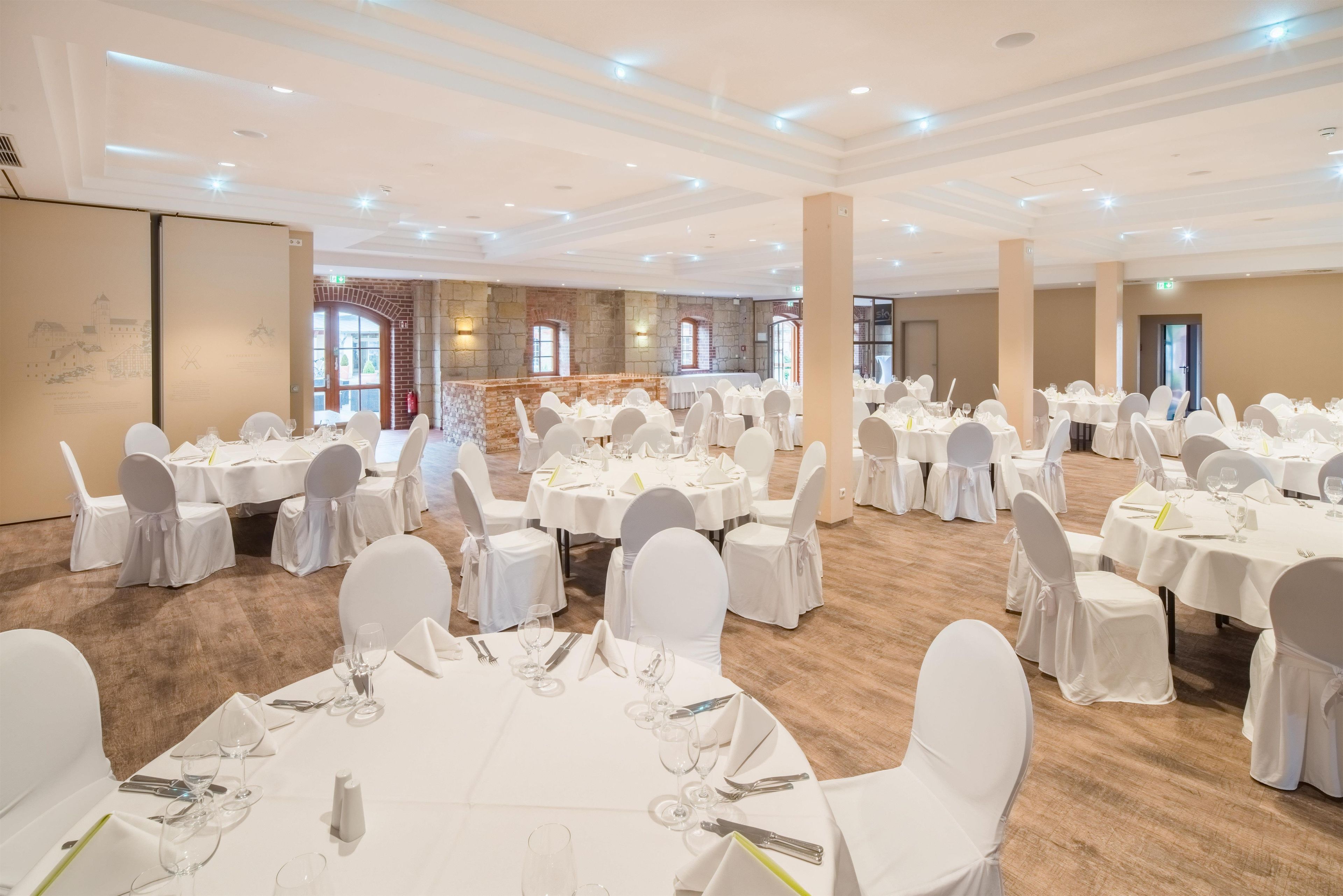 A banquet hall with round tables, white chairs, and a stone wall backdrop.
