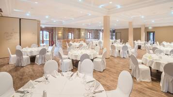 A banquet hall with round tables, white chairs, and a stone wall backdrop.