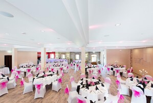 Ein geräumiger Festsaal mit runden Tischen und Stühlen, ausgestattet mit Kristalllüstern und einer Bar.