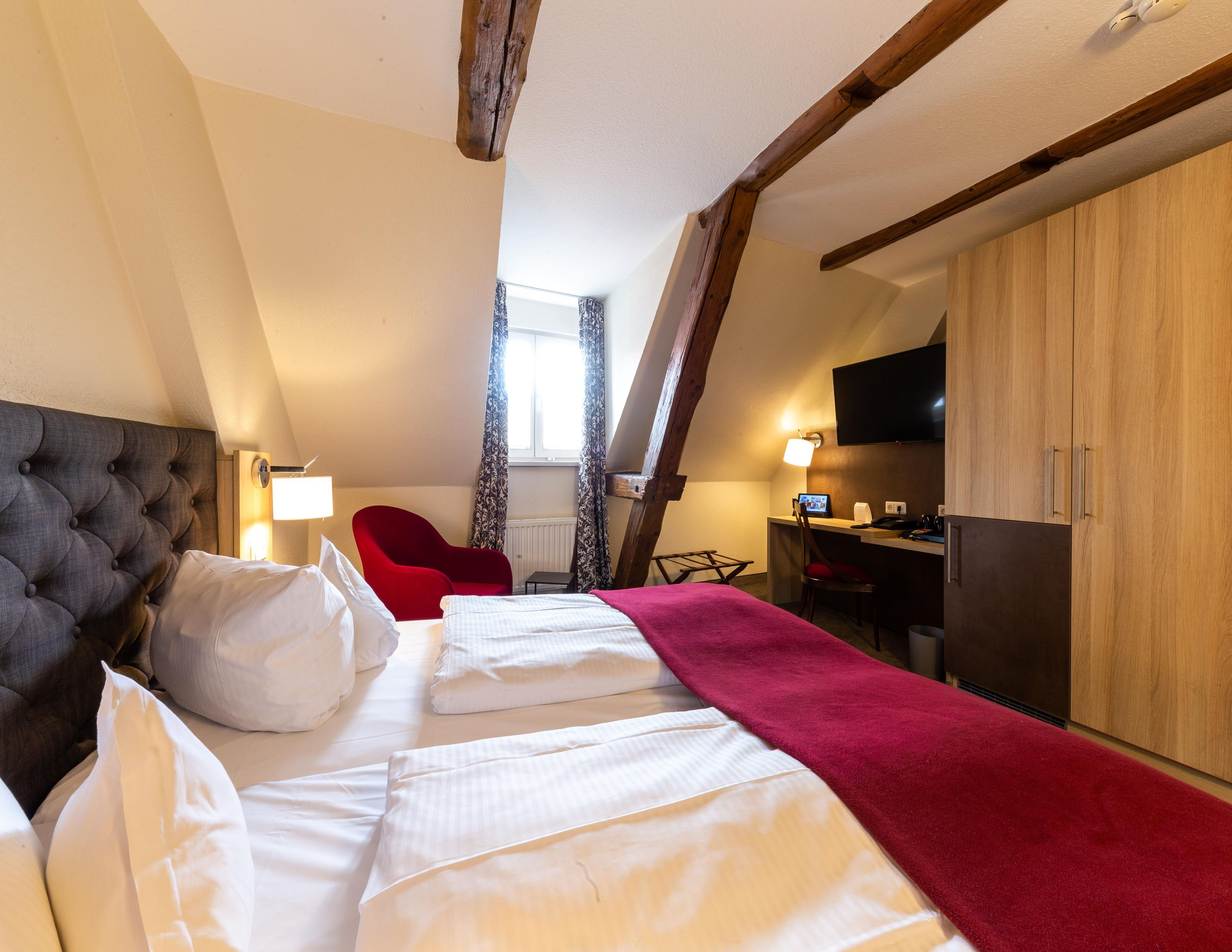 A hotel room with a large bed, a desk, a chair, and a television.