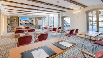 A conference room with tables, chairs, a projection screen, and a stone wall with a view of buildings.