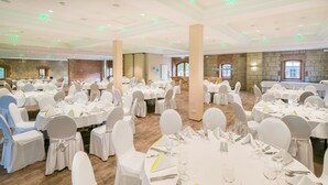 A banquet hall with round tables set for dining, white chairs, and a stone wall backdrop. - Best Western Hotel Schlossmuehle (Quedlinburg)