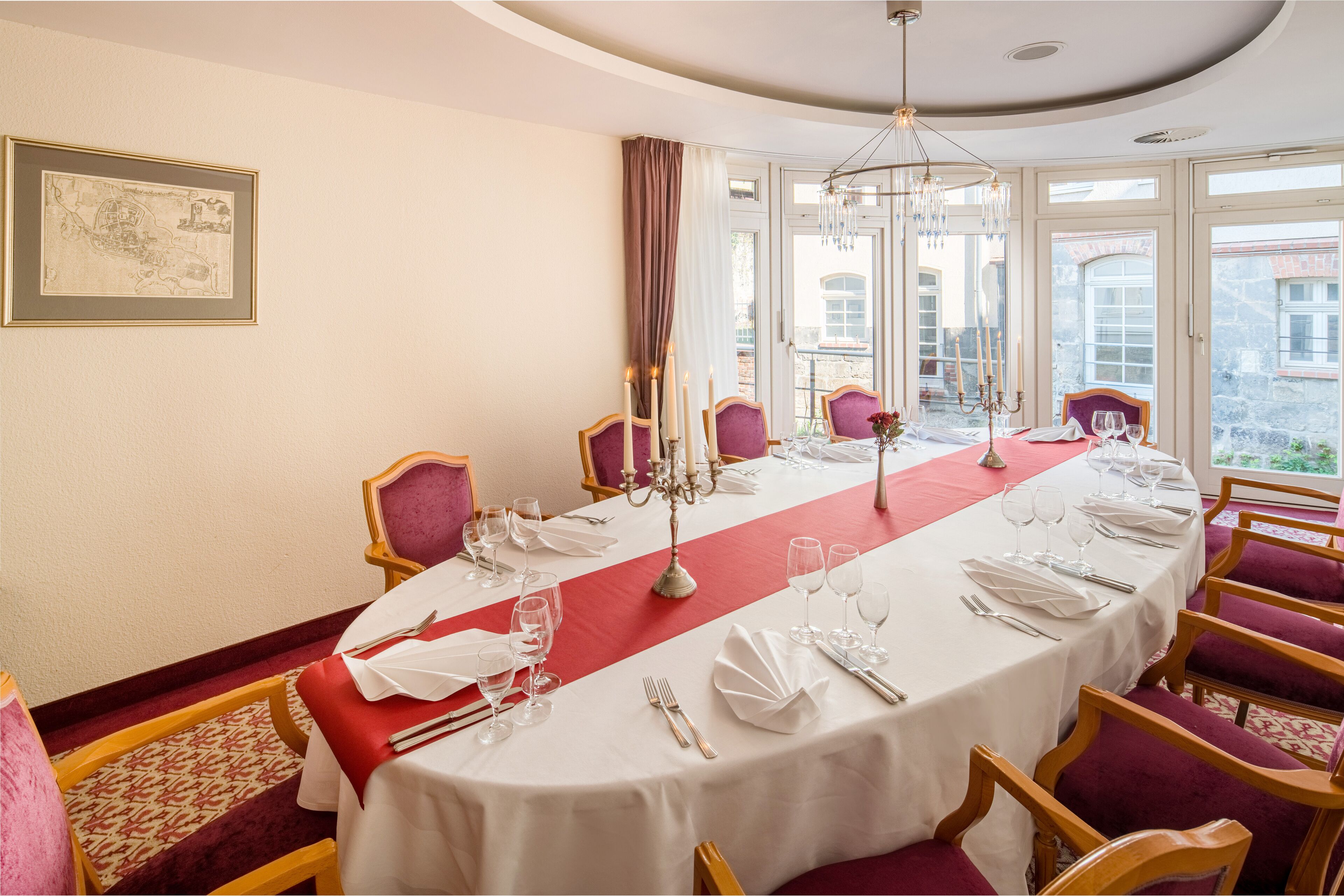 Een eetkamer met een lange tafel gedekt voor zes personen, rode en witte tafelkleden en een kroonluchter.