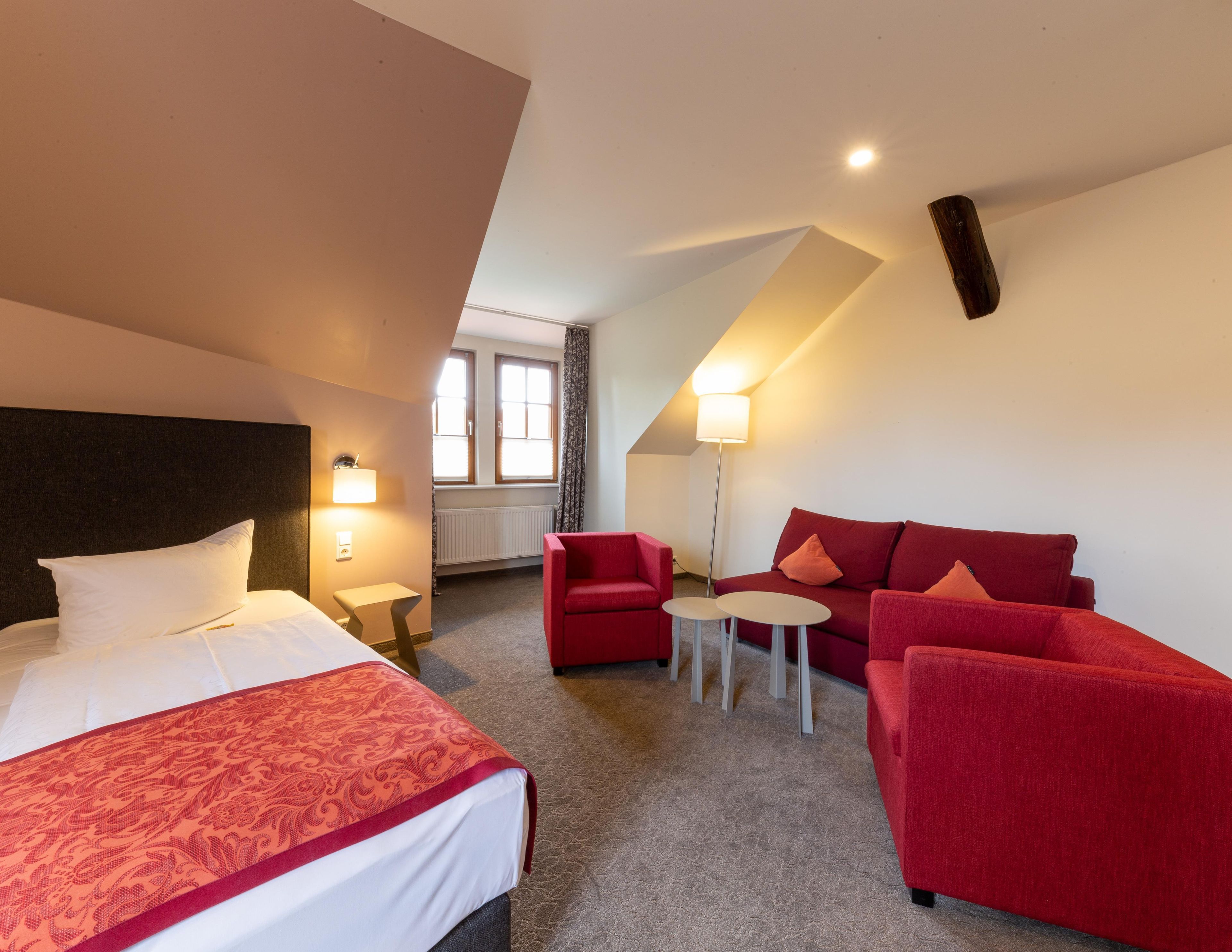 Ein Hotelzimmer mit einem Bett, einem roten Sofa, einem kleinen Tisch und einer Lampe.