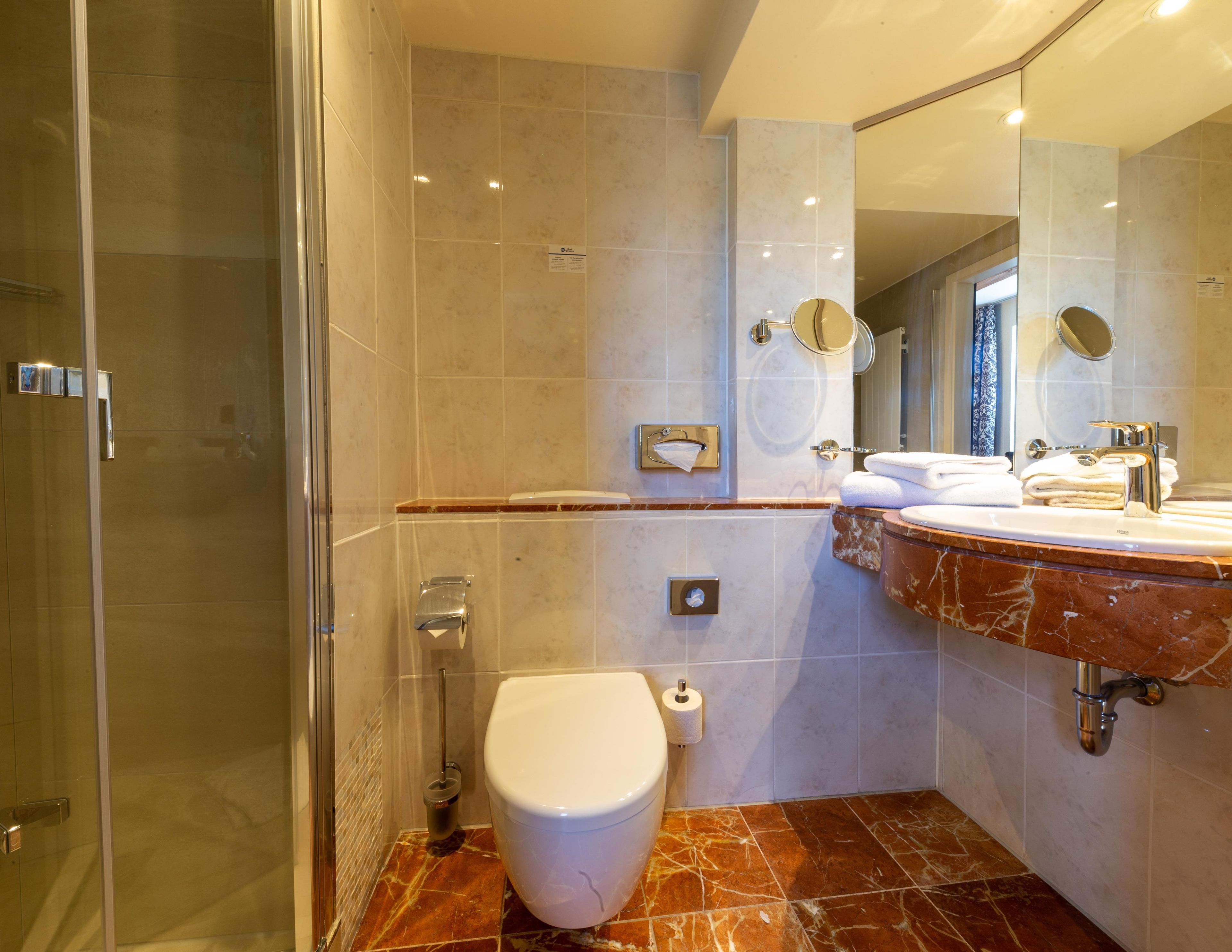 Un bagno moderno con doccia vetro, servizi igienici e lavabo con piano in marmo.