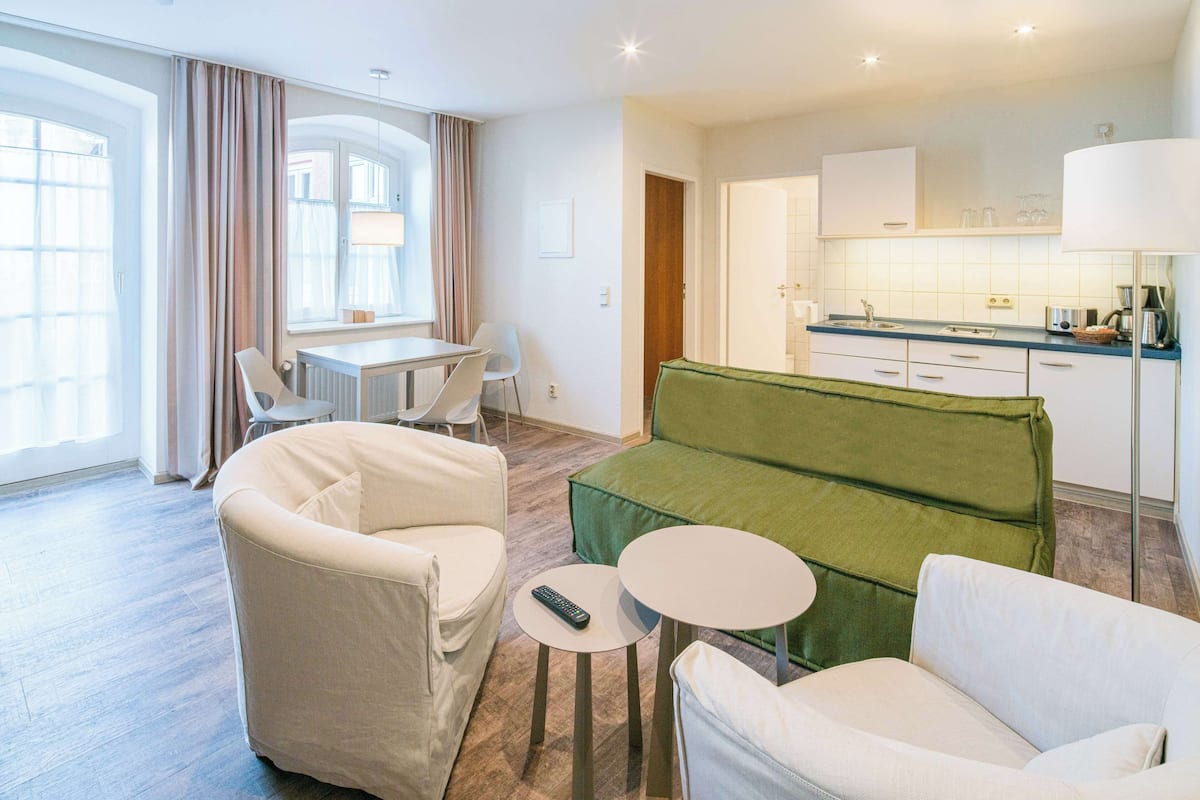 Un salon moderne avec un canapé vert, des fauteuils blancs et une petite table sur laquelle se trouve une télécommande.