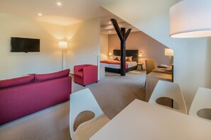 Una habitación de hotel moderna con una televisión de pantalla plana, un sofá rojo, una cama con ropa de cama blanca, un escritorio con una silla y un ventanal grande.