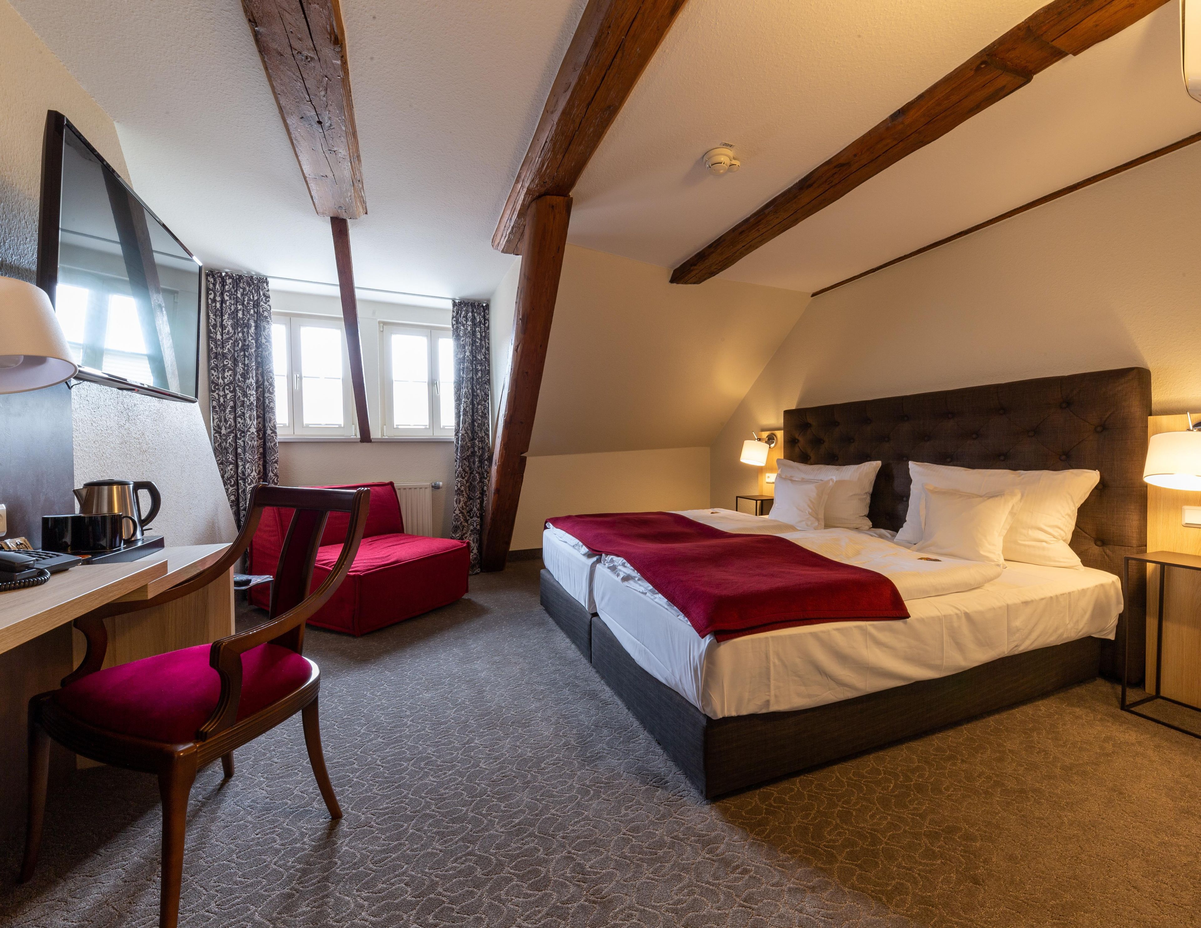 A hotel room with a bed, desk, chair, and a window with curtains.