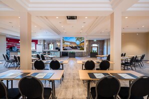 Un salón de conferencias con mesas y sillas, una zona de cocina y vistas a un patio con mobiliario exterior.