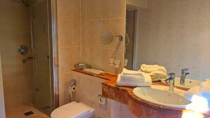 A bathroom with a glass-enclosed shower, a toilet, a sink with a marble countertop, and a mirror. - Best Western Hotel Schlossmuehle (Quedlinburg)