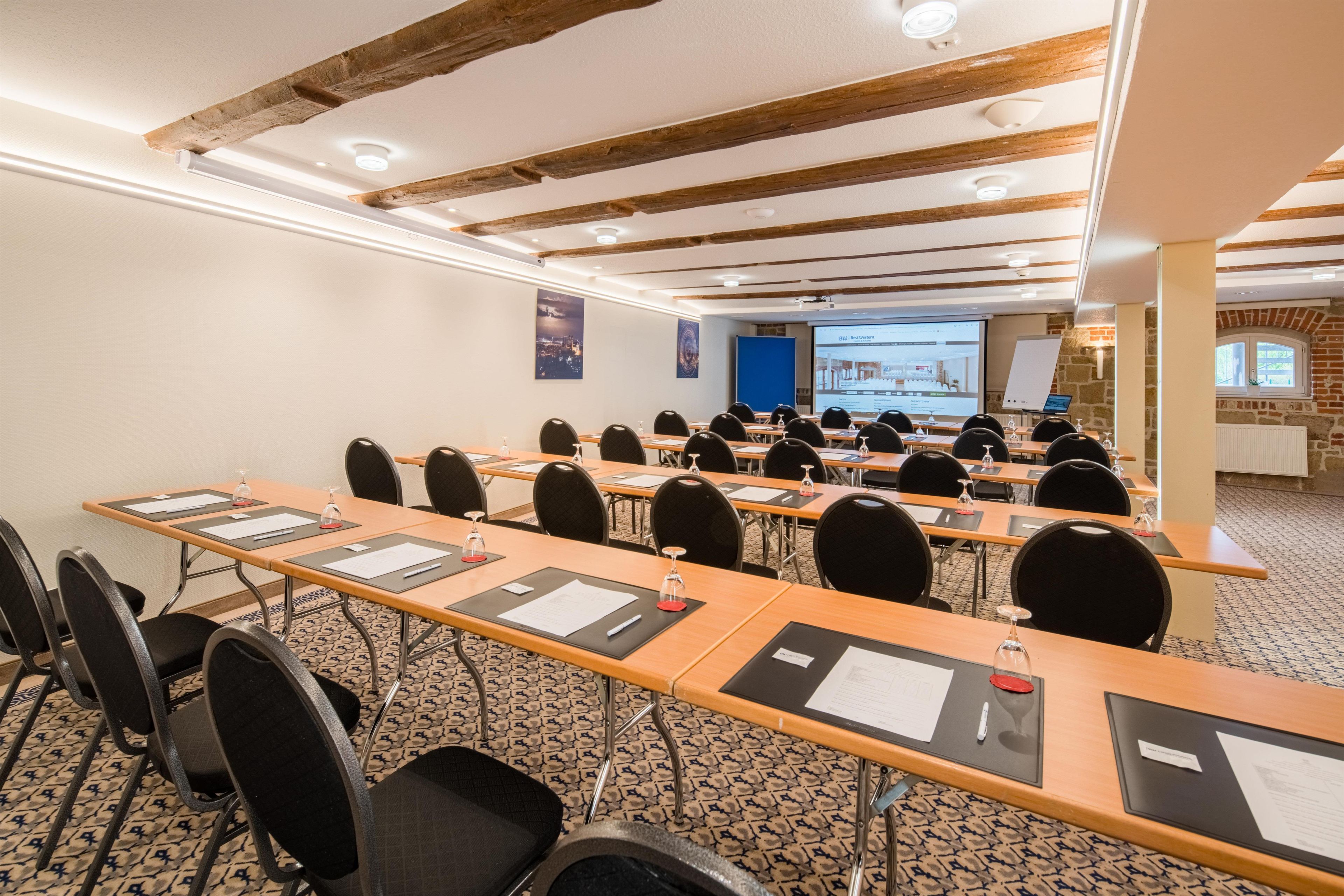 Une salle de conférence équipée de longues tables, de chaises et d’écrans de présentation.
