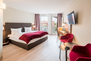 A hotel room with a bed, a desk, a chair, a TV, and a view of buildings through a door. - Best Western Hotel Schlossmuehle (Quedlinburg)