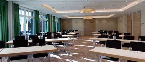 A conference room with multiple tables and chairs, large windows with green curtains, and a patterned carpet.