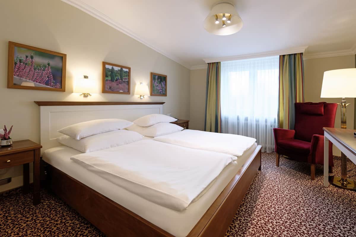 A hotel room with two beds, a desk, a chair, and a lamp.