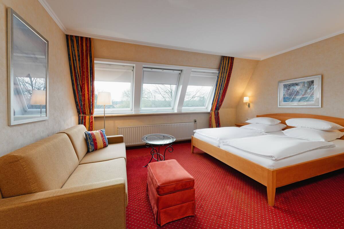 A hotel room with a bed, a sofa, a small table, and a window with curtains.