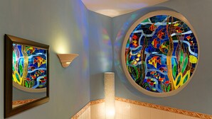 A bathroom with two stained glass windows depicting colorful fish, a wall-mounted light fixture, and a framed artwork. - Ringhotel Sellhorn (Hanstedt)