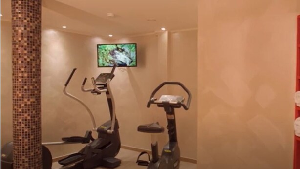 A gym with two exercise bikes, a television mounted on the wall, and a shelf with towels. - Best Western Plus Residenzhotel Lueneburg (Lueneburg)