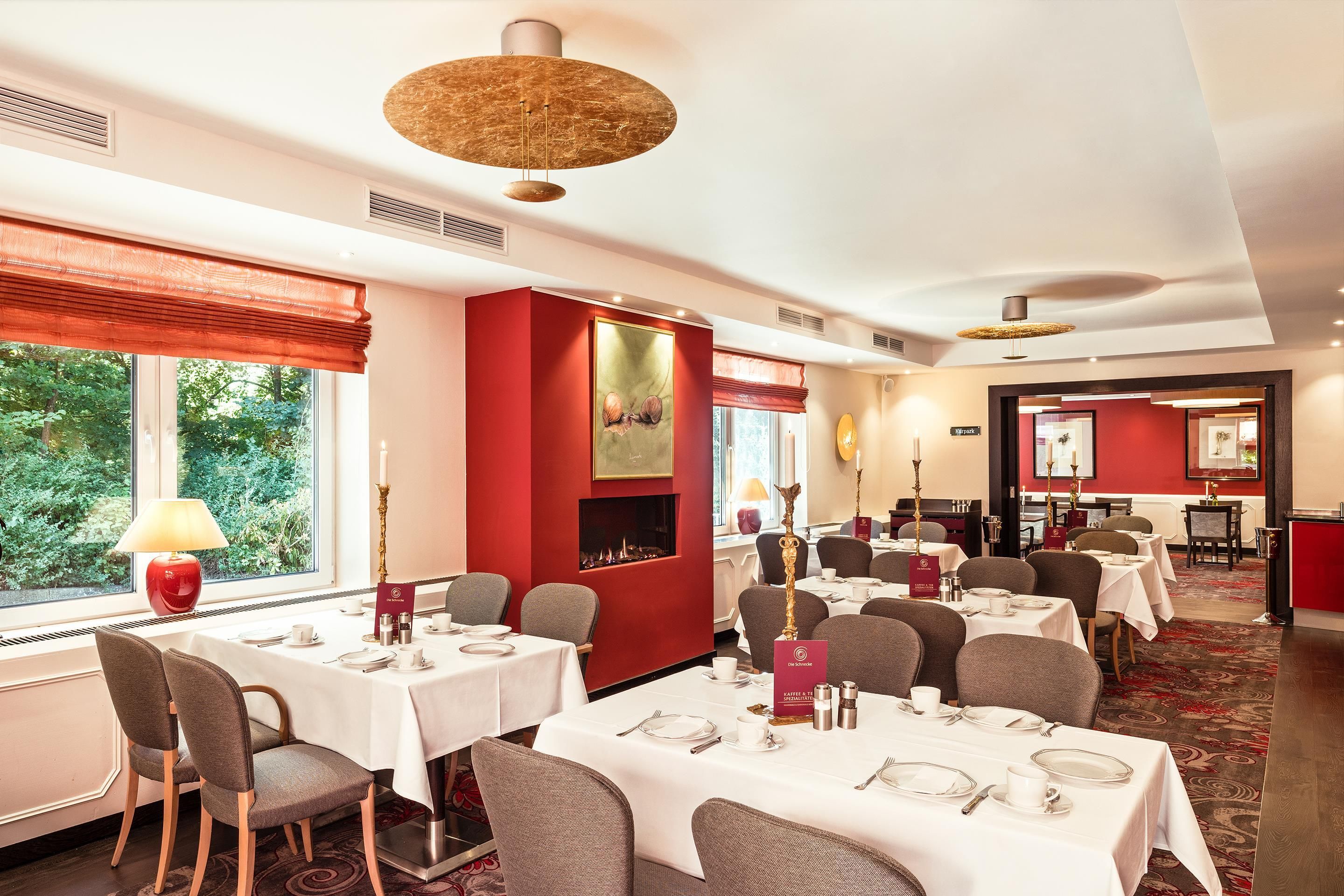 Een restaurantgedeelte in een hotel met gedekte tafels, een open haard en uitzicht op groen.