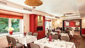 Een restaurantgedeelte in een hotel met gedekte tafels, een open haard en uitzicht op groen.