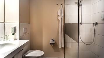 A bathroom with a toilet, a sink, a shower, and a towel hanging on the wall.