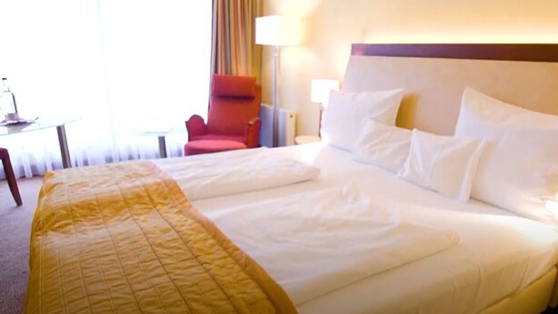 A hotel room with a large bed, a red armchair, a bedside table, and a lamp. - Best Western Plus Residenzhotel Lueneburg (Lueneburg)