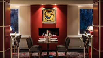 Un comedor con una mesa preparada para dos personas, una chimenea y un cuadro grande en la pared.