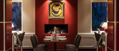 A dining room with a table set for two, a fireplace, and a large painting on the wall.