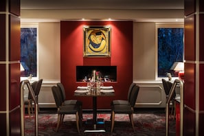 Un comedor con una mesa preparada para dos personas, una chimenea y un cuadro grande en la pared.