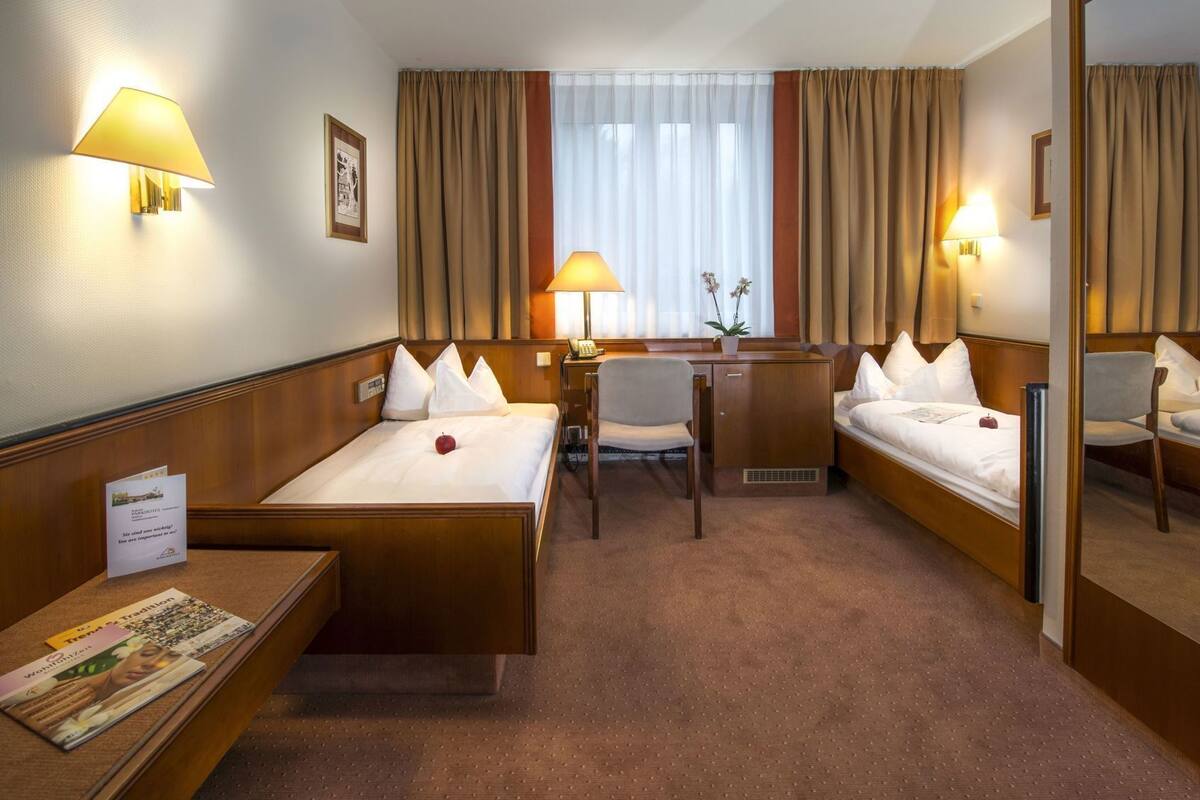 Une chambre d’hôtel avec deux lits simples, un bureau avec une chaise, une petite table avec des brochures et un miroir.