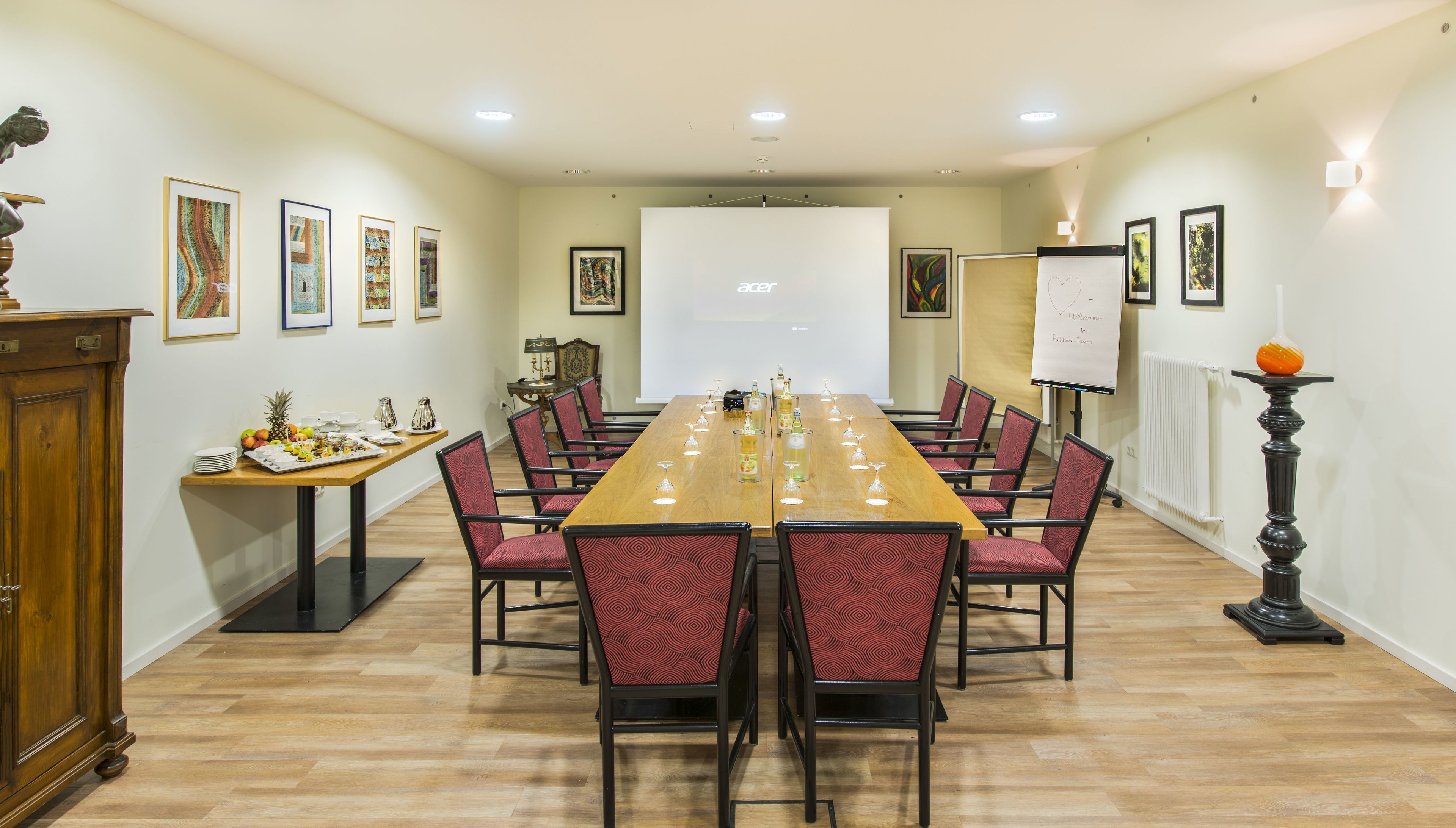 A conference room with a long table, red patterned chairs, a whiteboard, and framed artwork on the walls.