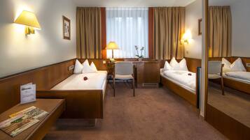 Habitació d'hotel amb dos llits individuals, una escriptori amb una cadira, una taula petita amb una poma vermella i un mirall.