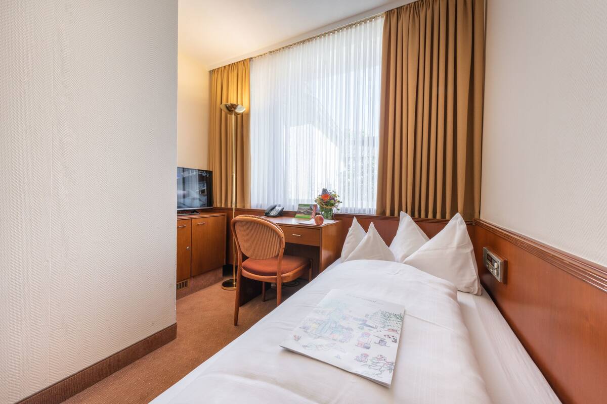 Une chambre d’hôtel équipée d’un lit, d’un bureau, d’une chaise, d’une télévision et d’une fenêtre avec des rideaux.