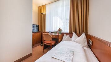 Ein Hotelzimmer mit einem Bett, einem Schreibtisch, einem Stuhl, einem Fernseher und einem fenster mit Vorhängen.