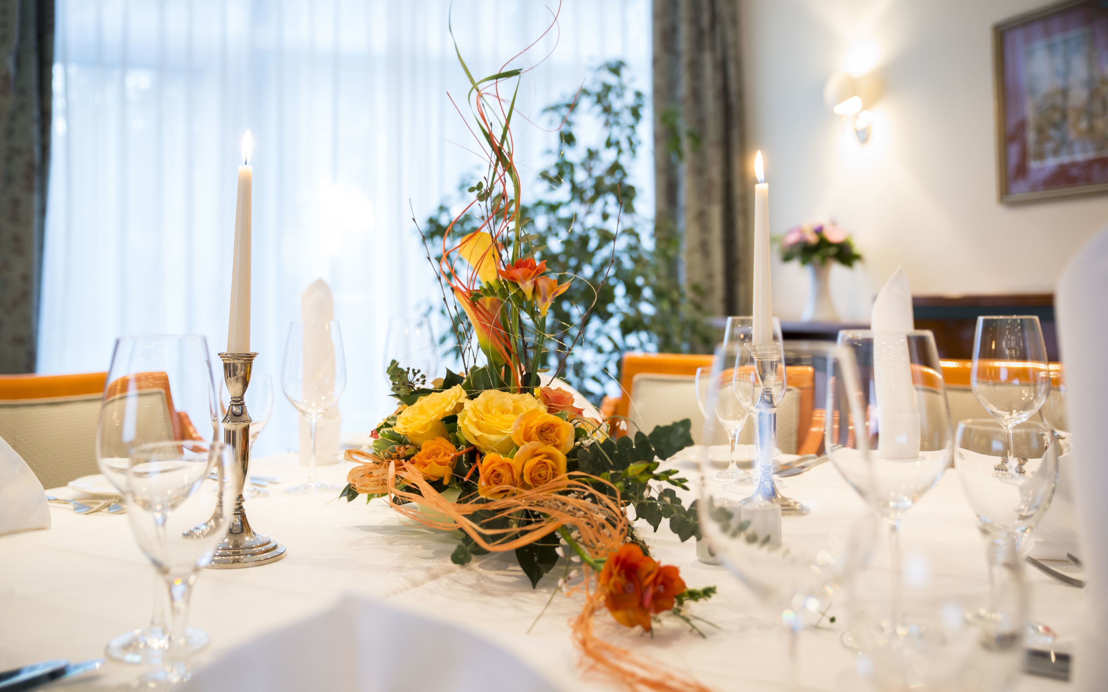 A dining table set with candles, glasses, and a floral centerpiece.