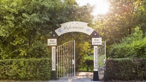 Une entrée fermée par un portail, sur laquelle est apposée une enseigne indiquant « Hufschmiede », et de part et d’autre, deux autres enseignes indiquant « Biergarten ».