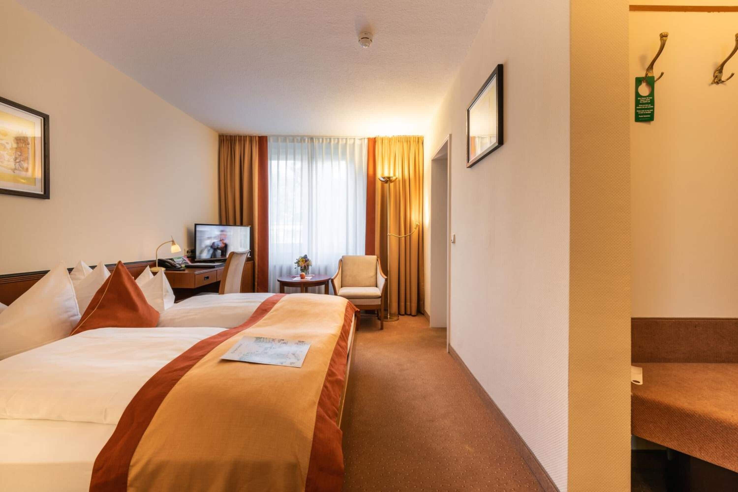 Habitación de hotel con dos camas, un escritorio con televisor, una silla y una mesita con un florero.