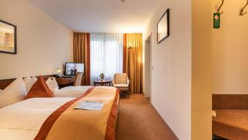 Habitación de hotel con dos camas, un escritorio con televisor, una silla y una mesita con un florero.