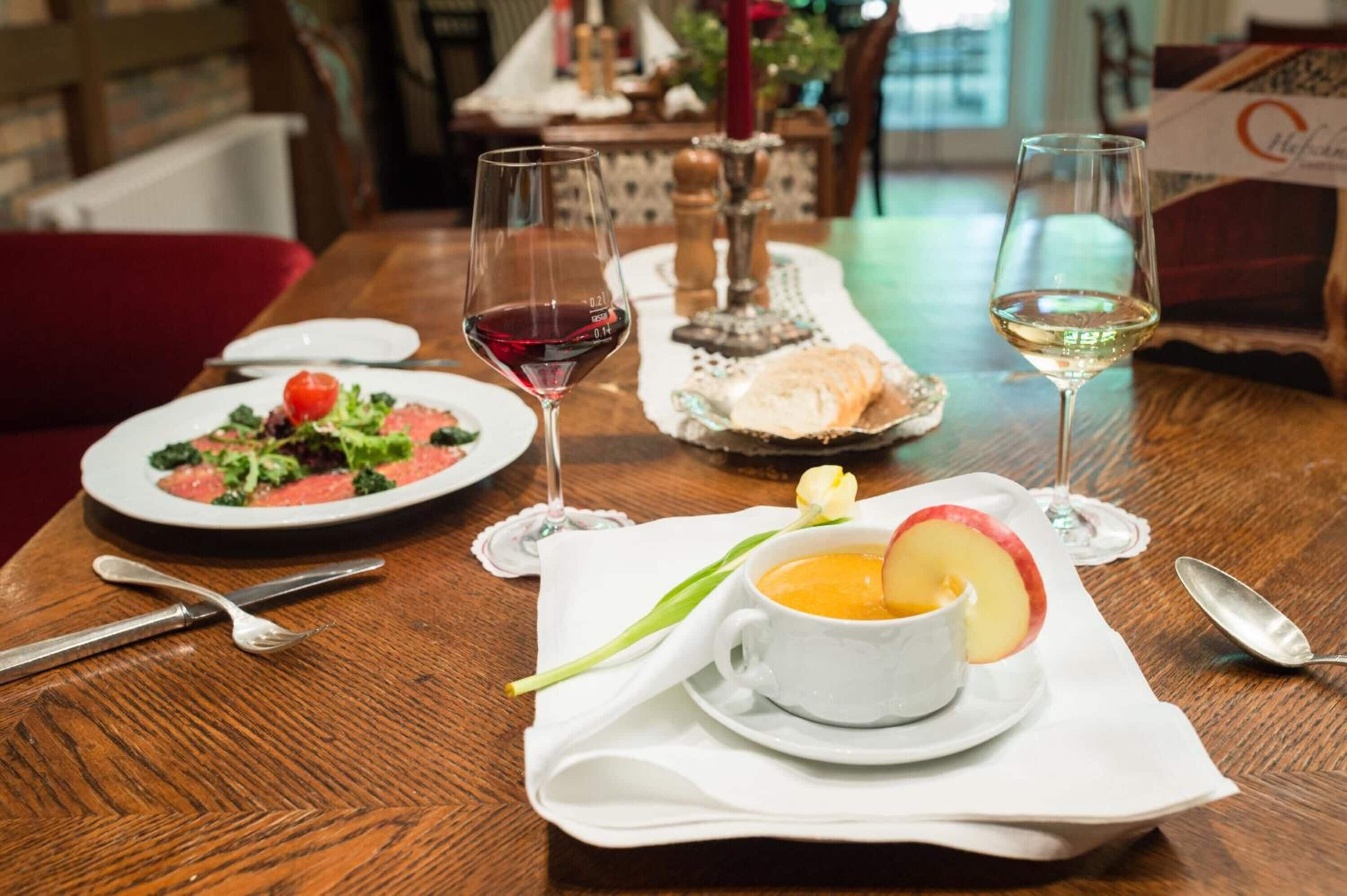 Une table à manger avec des assiettes remplies de nourriture, des verres de vin et une tasse de soupe.