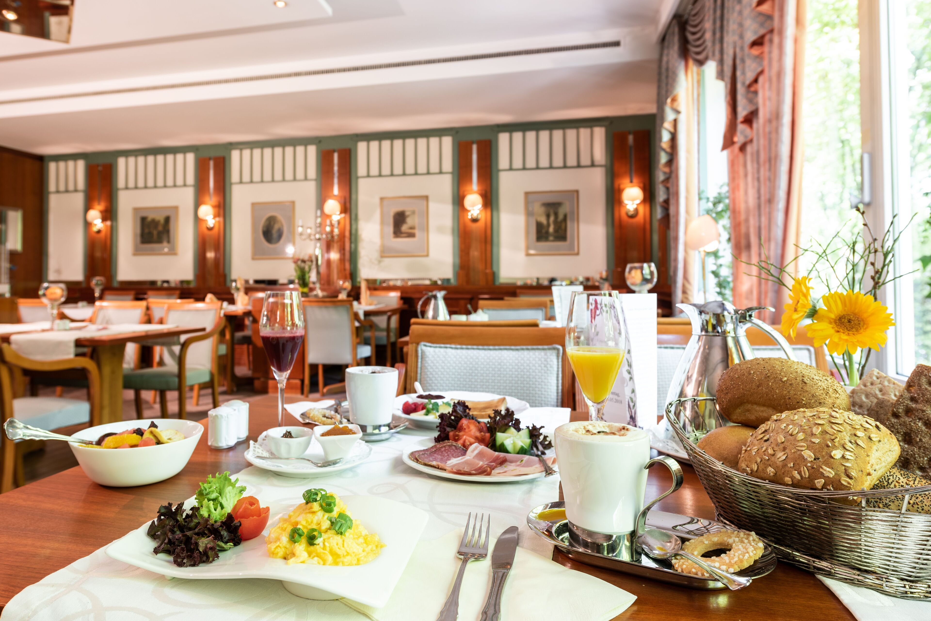 A breakfast setting with a table set for two, including plates of food, a basket of bread, and a glass of orange juice.