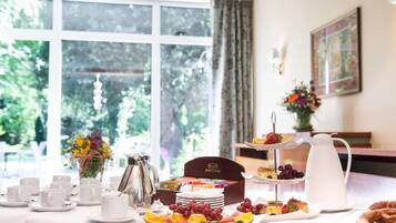 A breakfast setup with a variety of pastries, fruits, and a coffee pot on a table.