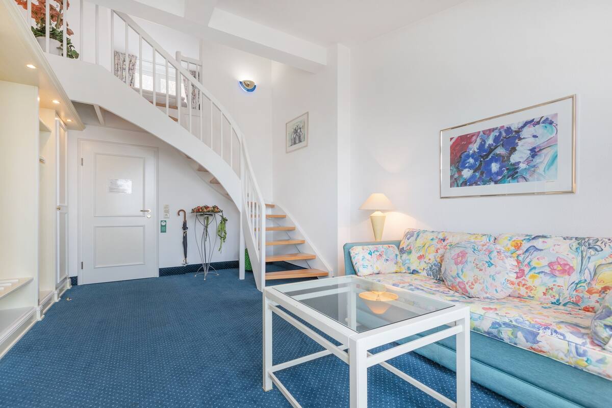 A living room with a staircase, a sofa with floral upholstery, and a glass coffee table.