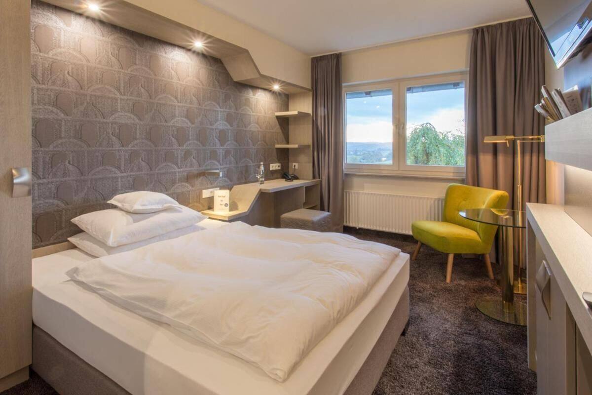 A hotel room with a large bed, a desk, a chair, a window with a view, and a modern headboard.